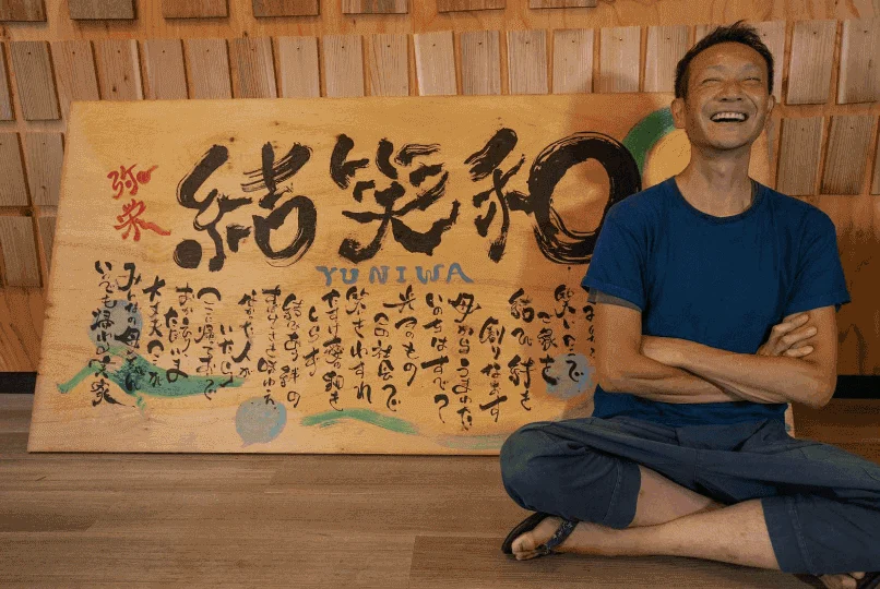 「結笑和」の看板の前で笑う黒川洋司さん